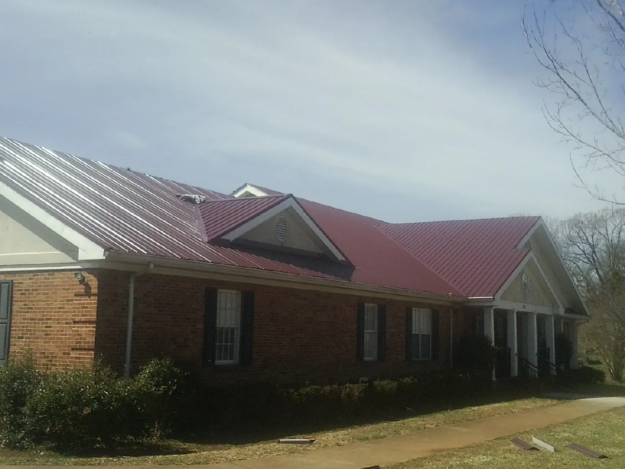 Red metal roof with gabled entries on a long brick building, from a Hail Damage Roof Repair job in Mount Gilead