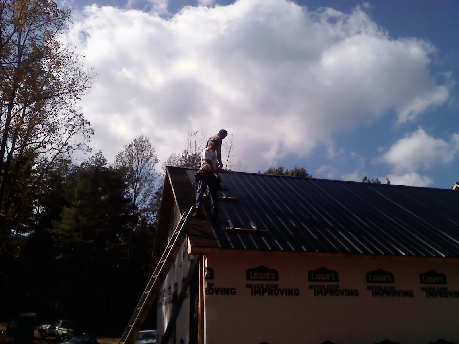 Roofer fastening dark metal panels high against a cloudy sky, from a Roof Inspection job in Mount Gilead