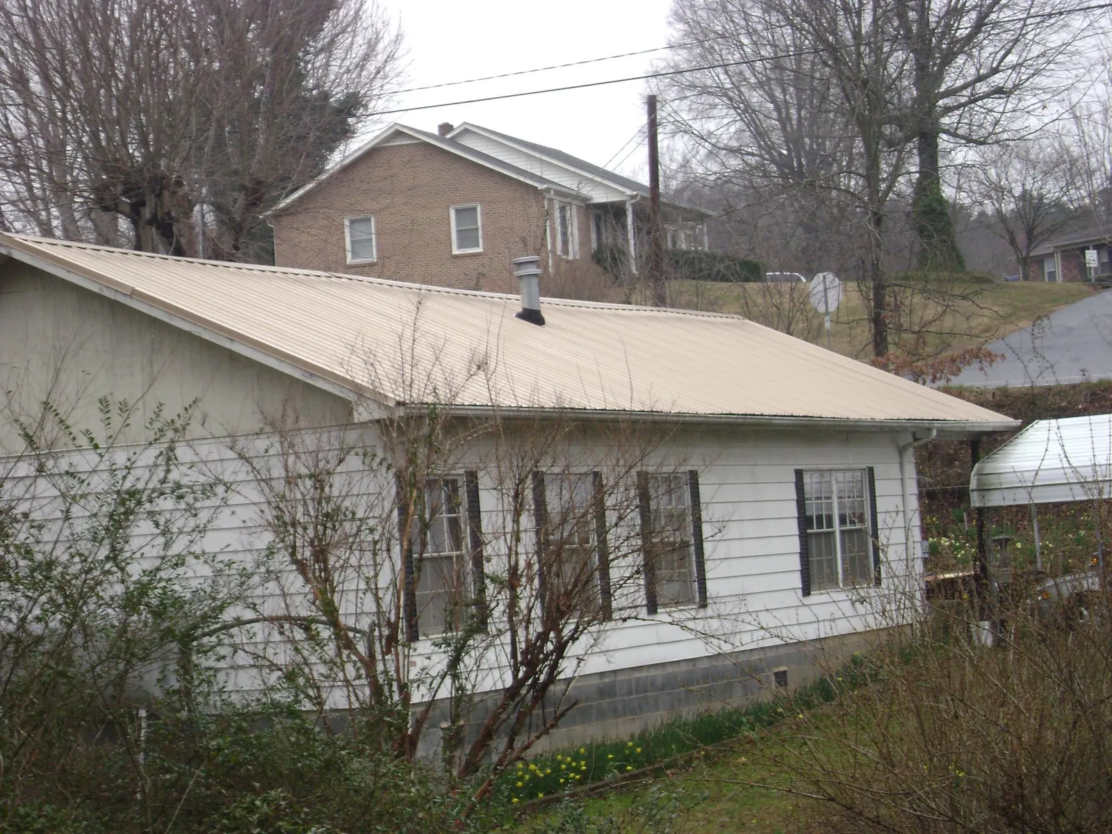 Tan metal roof on a white sided house set into a hillside — Commercial Roofing by Roofing Brothers in Mount Gilead